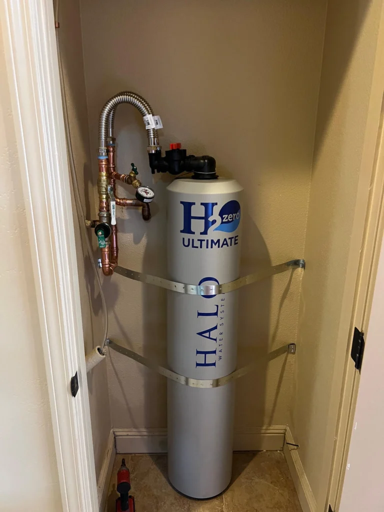 A water filtration system labeled "H2 zero ULTIMATE HALO" is installed in a small closet, secured with metal straps and connected to pipes. This setup would make an excellent addition to any photo gallery showcasing innovative home solutions.