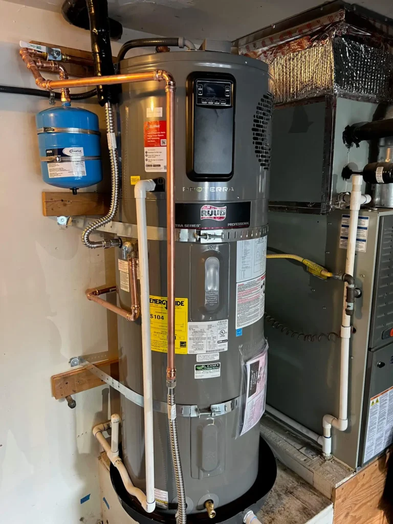 A gray electric water heater with connected pipes and labels is installed next to a furnace in a utility room with visible wiring and tubing, as seen in the Photo Gallery.