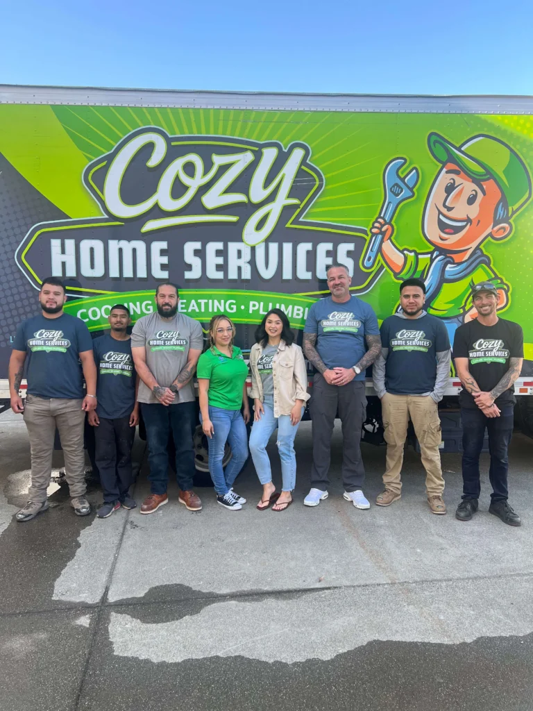 Eight people stand in front of a Cozy Home Services truck with a bright green sign, posing for a group photo on a sunny day—an image perfect for the company’s photo gallery.