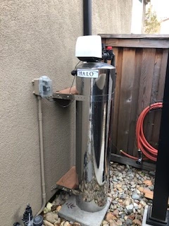 A stainless steel water filtration system labeled "HALO" is installed next to a beige wall, with rocks and a red hose visible nearby, showcasing the benefits of reverse osmosis for clean water.