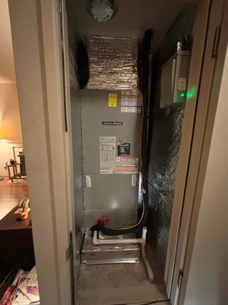 A central air conditioning unit installed in a small closet, with pipes, wiring, and foil insulation visible around the system—perfect for showcasing in a photo gallery of home improvement projects.