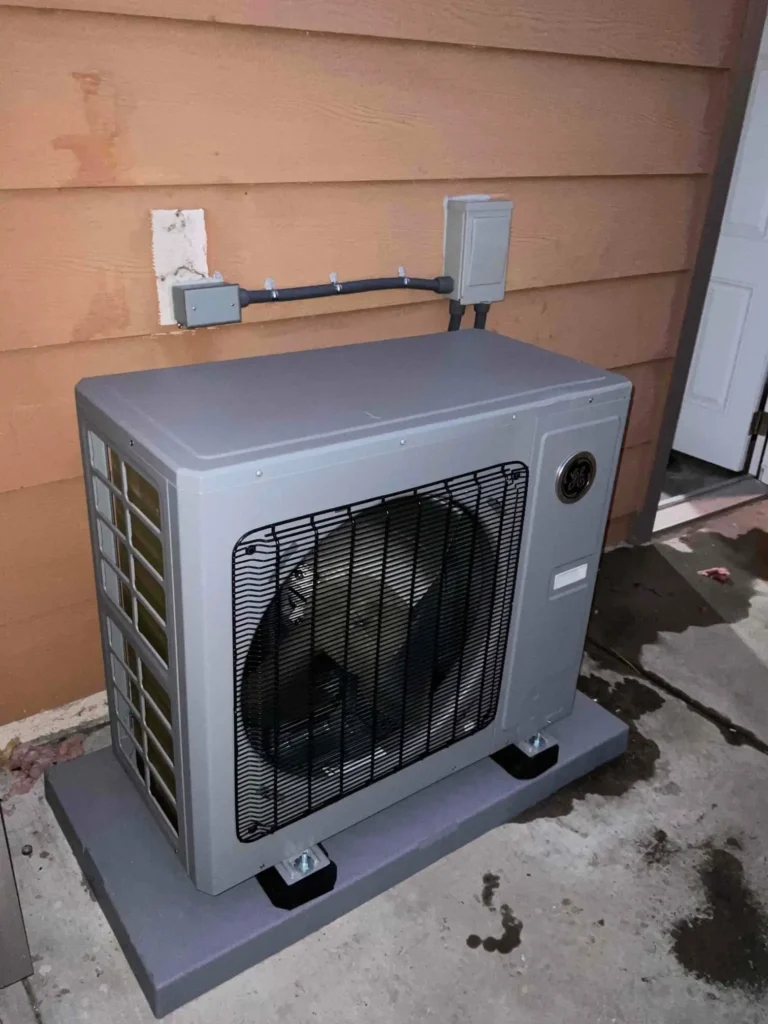 Photo gallery showcasing an outdoor air conditioning unit installed on a concrete pad next to a brown siding wall, with electrical box mounted above and visible wiring.