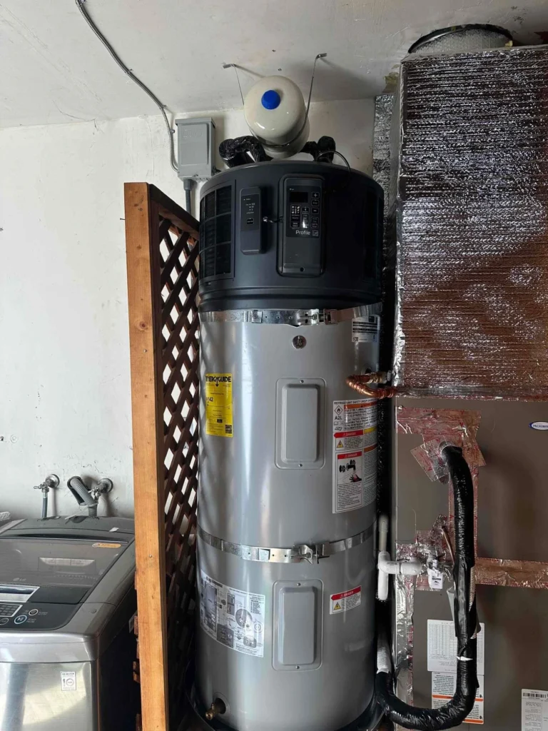 Tall gray water heater with warning labels installed in a utility area, next to a washing machine and HVAC unit, with a plastic jug placed on top—an everyday scene perfect for any home photo gallery.